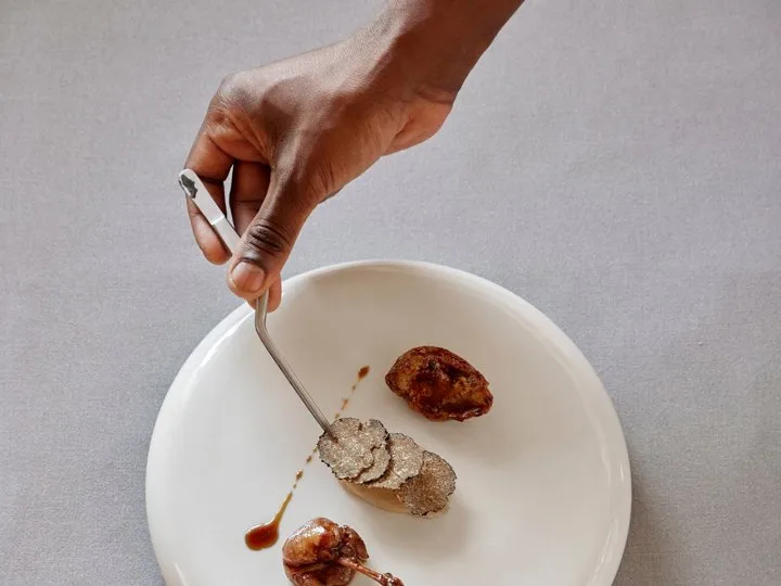 Chef arranging truffle slices with tweezers on a white plate with glazed meat